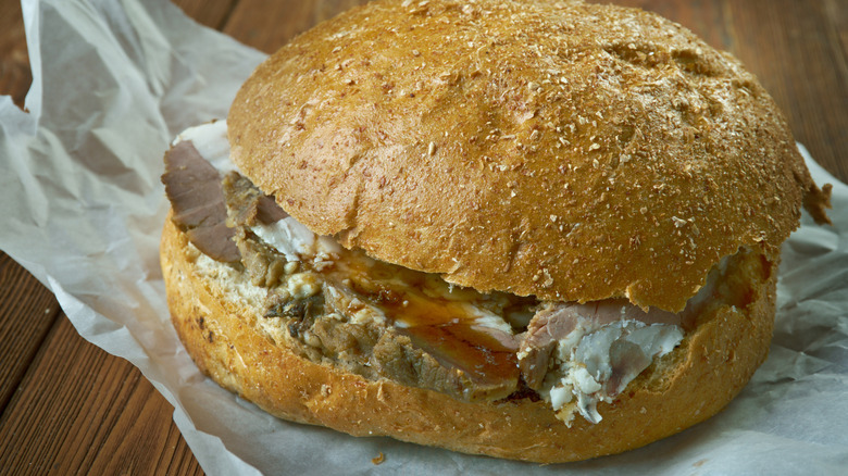 A beef on weck sandwich with horseradish sauce and au jus gravy on a paper wrap.