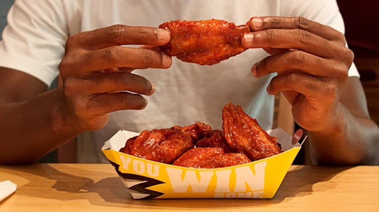 A person holds a chicken wing from a Buffalo Wild Wings meal on a table.