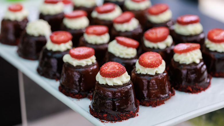 Pieces of chocolate cake with whipped cream and a strawberry on top sit on a plate at a buffet.