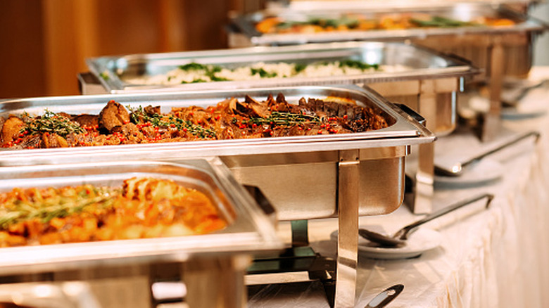 Metal tubs of food are set out on a buffet table in a row
