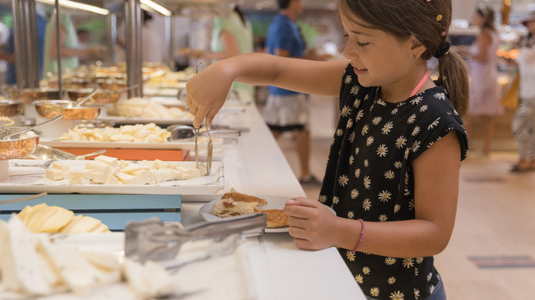 A young girl taking items from a buffet with tongs, and putting them on her plate.