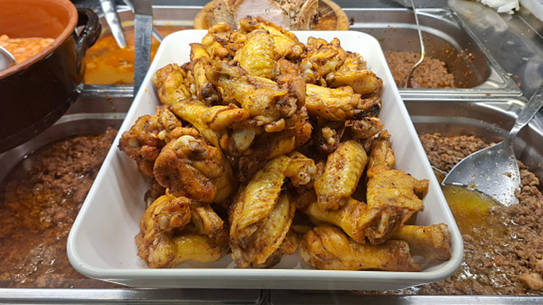 A tray of chicken wings sits out alongside other meats at a buffet.
