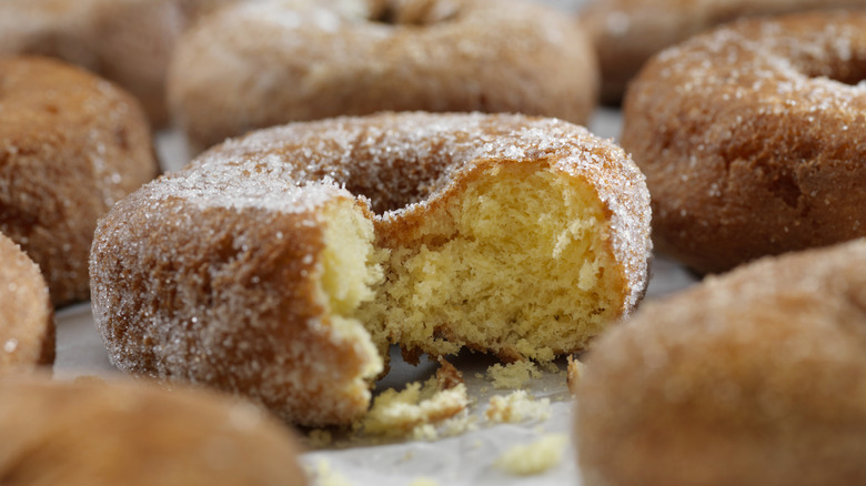 The picture focuses on a donut with a bite taken out of it, surrounded by several full donuts.
