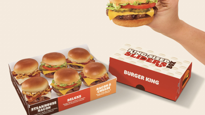 A hand holding burger king slider with six burger sliders in the box.