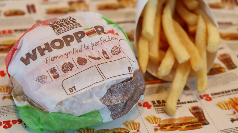 Wrapped Whopper Jr. and small French Fries sitting on BK coupons at a Burger King restaurant.