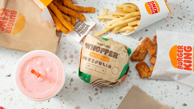 Burger King Whopper in paper wrapper with fries and a drink