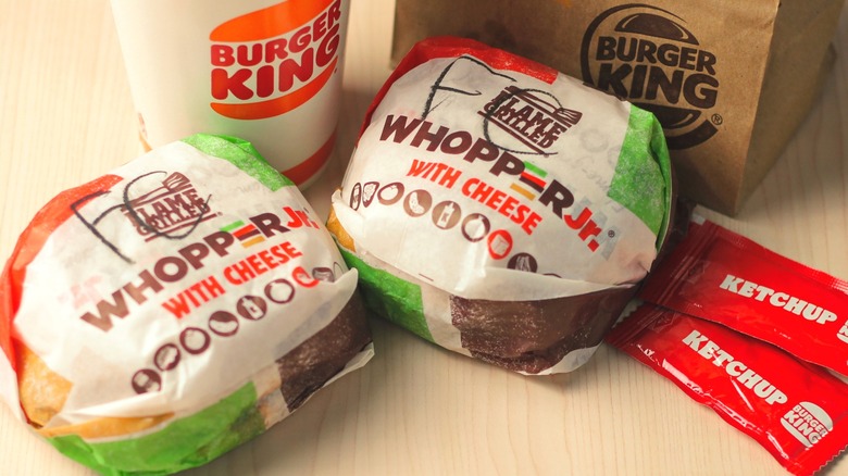 Two Whopper Jr. sandwiches with drink and ketchup packets nearby