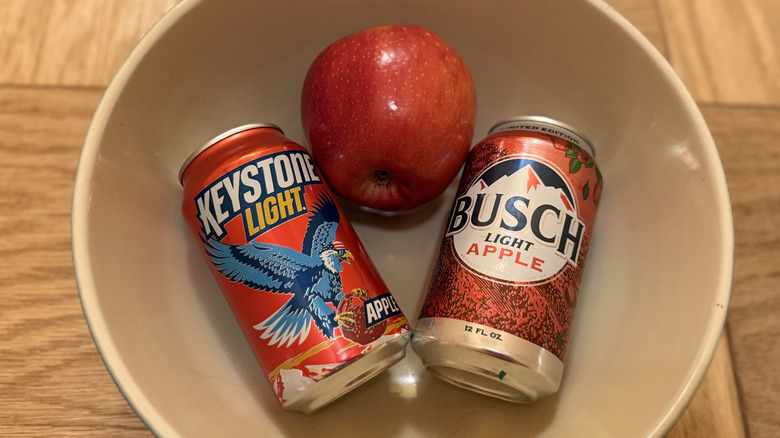 Two cans of apple beer and an apple sit in a bowl