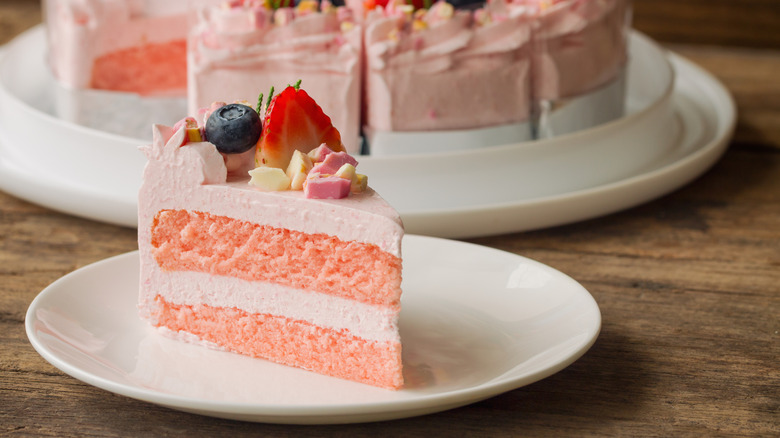 A strawberry pink piece of cake with fruit and pink icing sitting on a plate on a table.