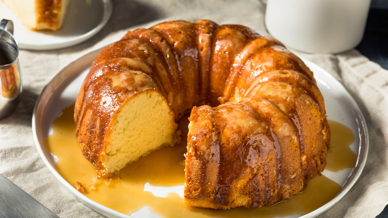 A buttered rum Bundt cake sitting on a white plate with sauce drizzled on top.