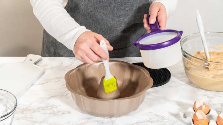 baker greases bundt cake pan with pastry brush and shortening