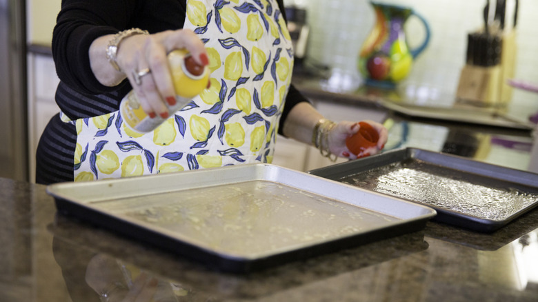 woman sprays cookie sheets with cooking spray