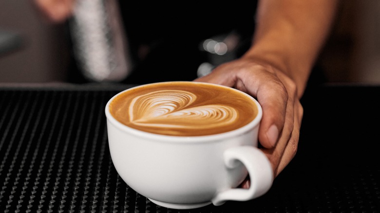 A barista's hand holding a latte