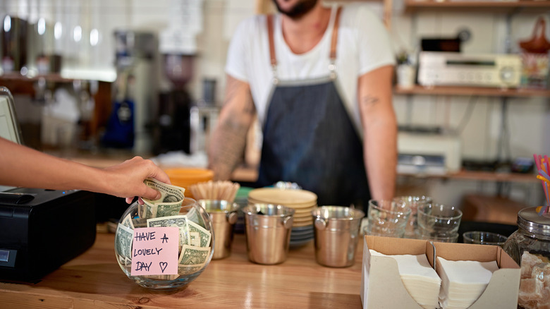 A person putting $2 in the tip jar at a cafe
