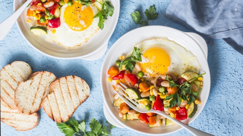 Two white plates with half of it cooked veggies, a quarter sunny side up egg, and 4 slices grilled bread on the side