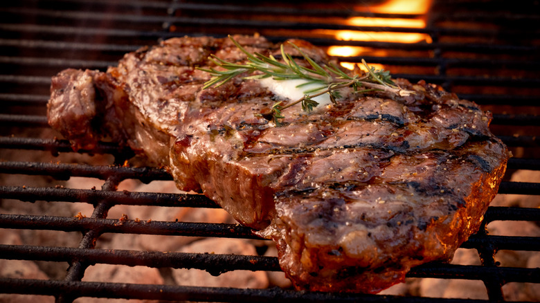 A juicy ribeye with a sprig of rosemary on the grill