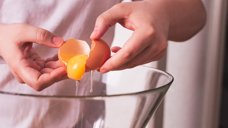 A person breaks an egg into a bowl