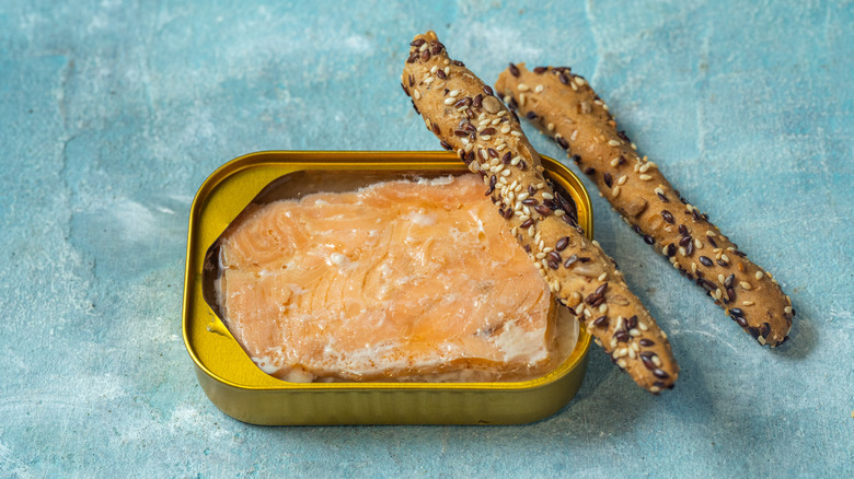 A pack of canned salmon with two seeded breadsticks on the side