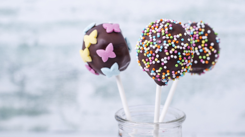 Chocolate coated cake pops in a glass jar covered in sprinkles