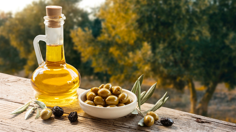 A small glass pitcher of olive oil and a bowl of olives