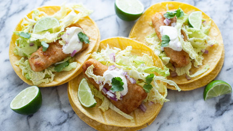 Three beer-battered fish tacos with shredded vegetables and lime