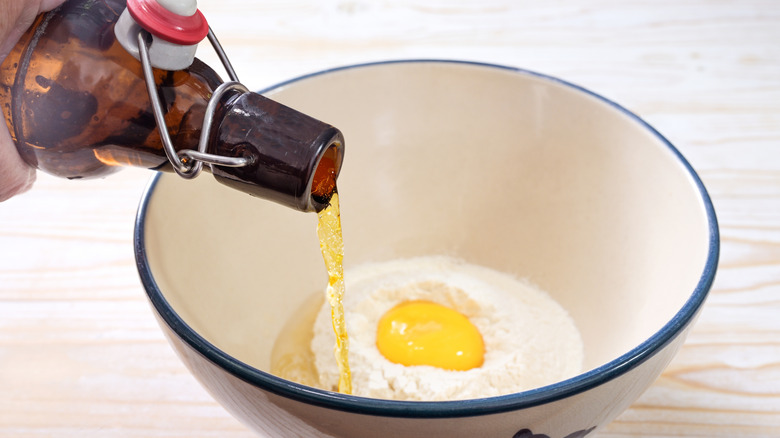 A bottle of beer being poured into a bowl of flour and egg