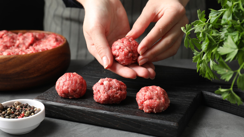 Person's hands making meatballs on a wooden board