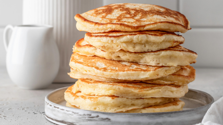 A very fluffy stack of pancakes on a marble plate on a white counter