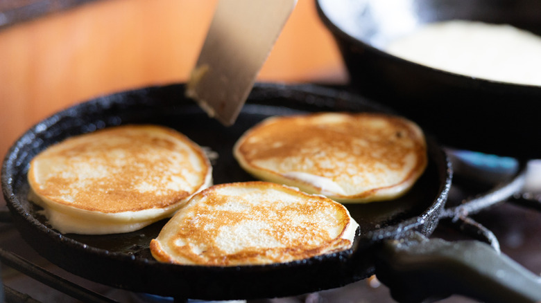 Three fluffy pancakes cooking in a cast iron skillet after the batter rested