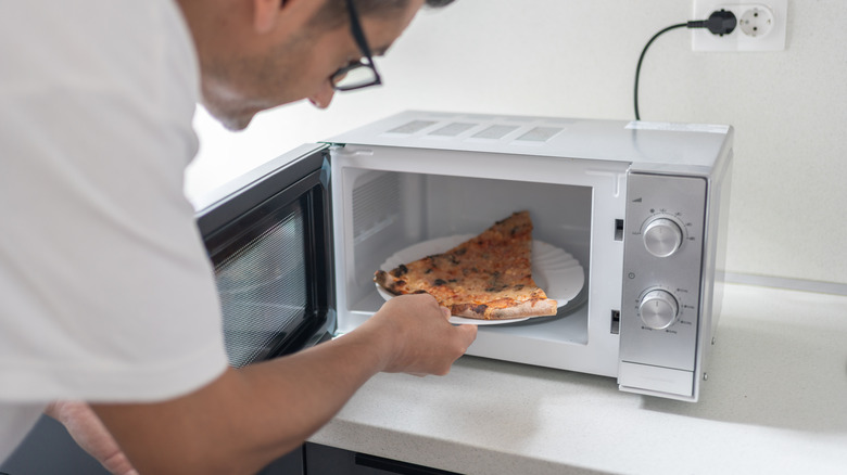 Man microwaving pizza on paper plate