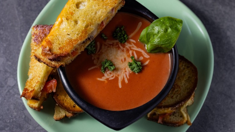 bowl of tomato soup with garnishes and sandwich on top