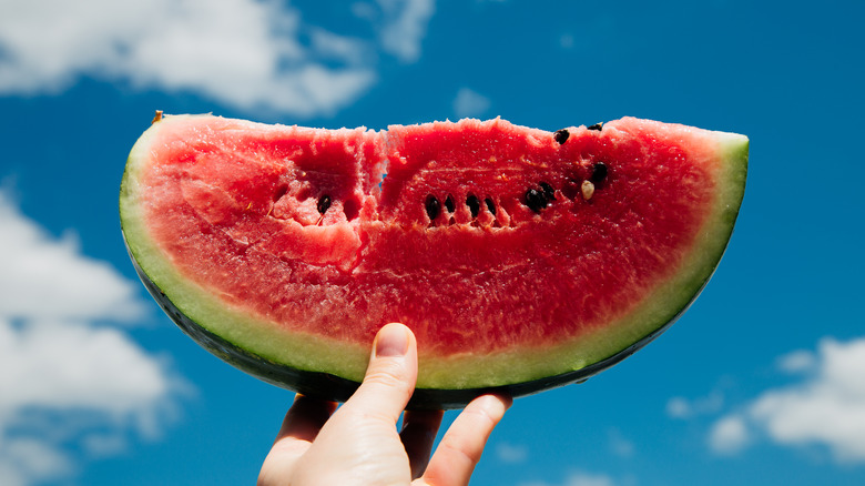 Someone holding up a lisce of watermelon against a blue sky