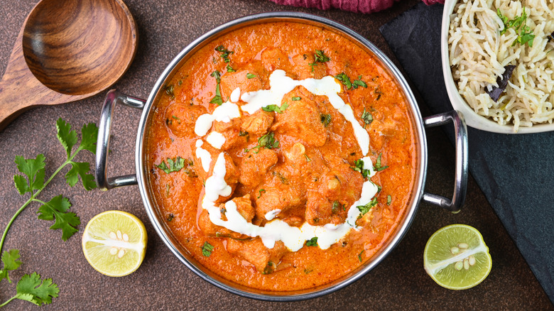 A dish of butter chicken curry with rice, lime, and yogurt