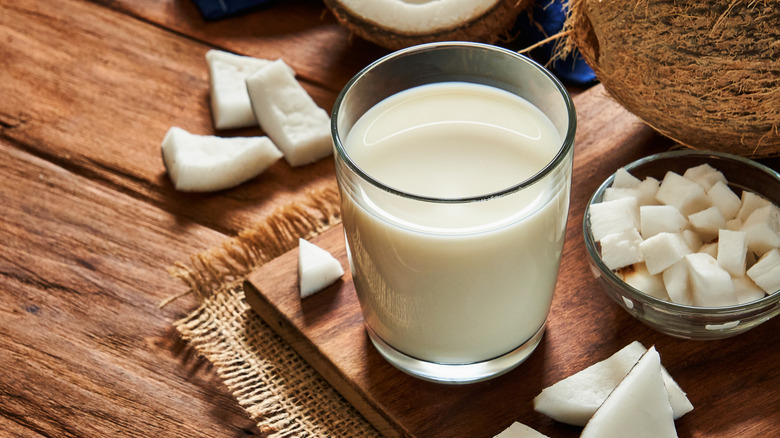 a glass of coconut milk on a cutting board surrounded by coconut chunks