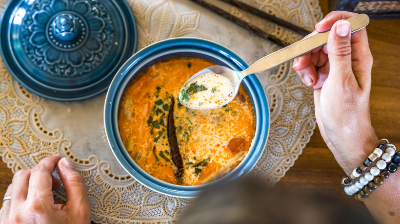 person holding spoon of thai curry above bowl