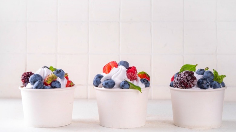 Three cups of frozen yogurt sitting on a surface with berries in them.