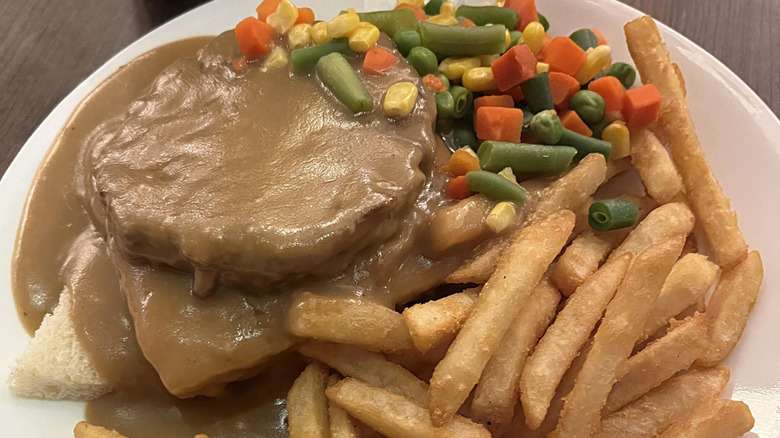 Canadian hot hamburger, fries, and veggies on a white plate in a diner.