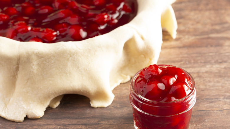 A jar of cherry pie filling and a filled pie shell