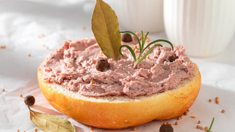 A half of a roll with meat spread and herbs atop it