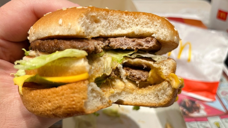 Person holding a McDonald's burger with a bite missing close-up.
