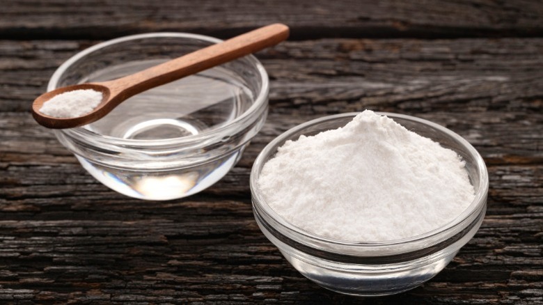 A bowl of baking soda next to a bowl of water.