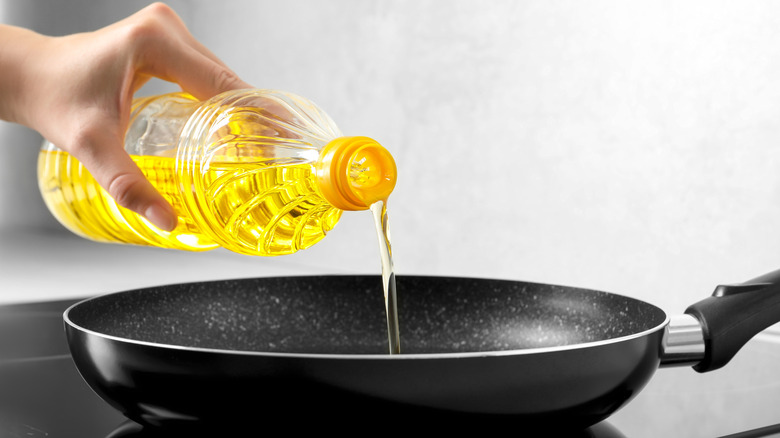 A person holding a bottle of vegetable oil and pouring some into a carbon steel pan