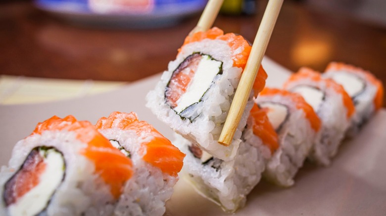 Chopsticks picking up a piece of salmon sushi roll