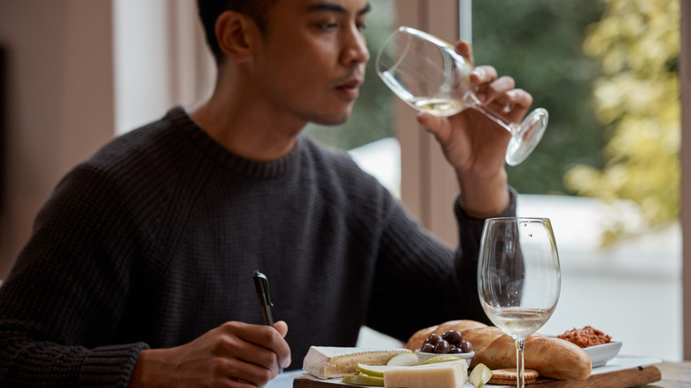A man drinking a glas on wine inside a restaurant and taking notes.