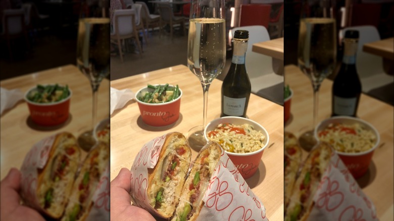 Someone raising up two sandwhich halves at a restaurant table holding additional food.