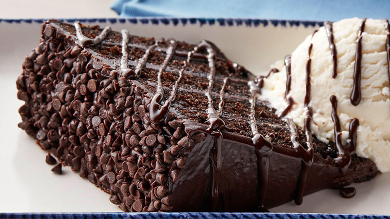 A closeup of a multi layered chocolate cake with fudge frosting served with vanilla ice cream and chocolate sauce