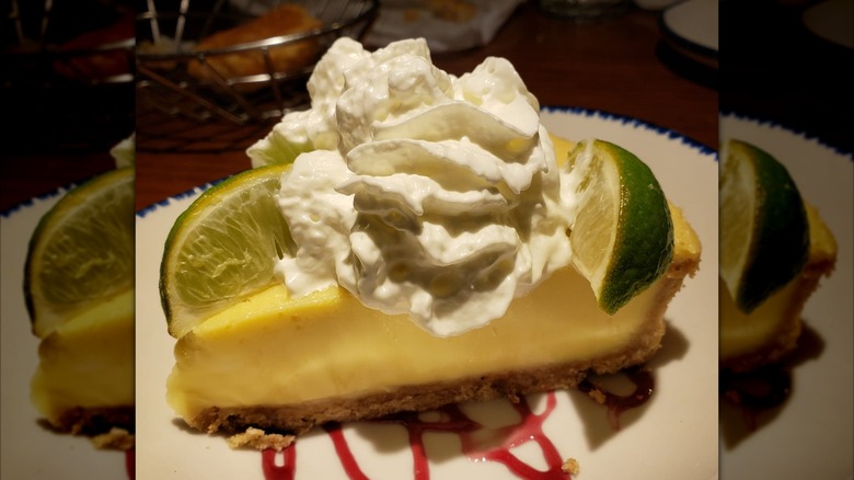 Slice of Key Lime pie with whipped cream and lime wedge on a white plate