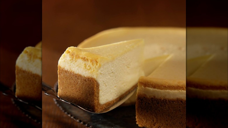 Side view of one slice of classic cheesecake being removed from the whole