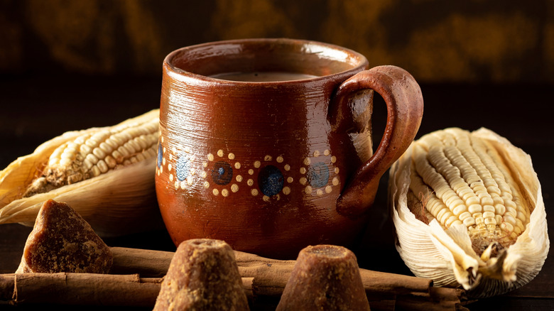 A Mexican mug is shown with an ear of corn and pieces of chocolate surrounding