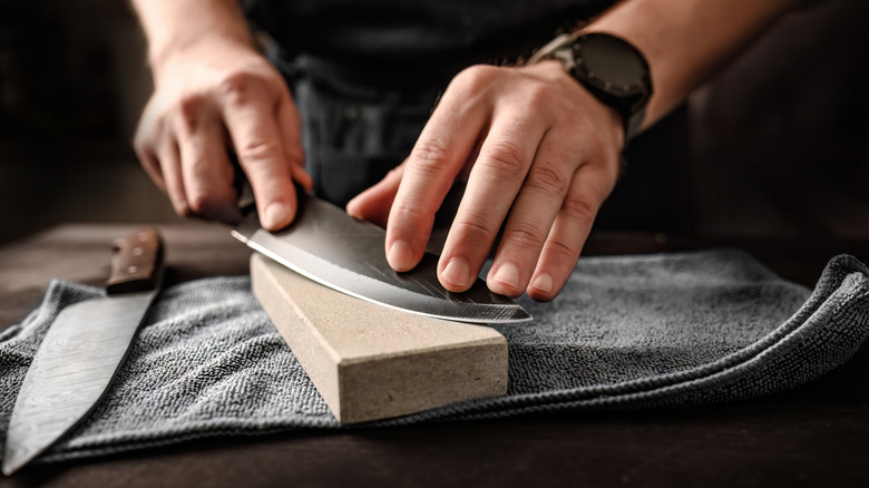 man sharpens chef's knife using whetstone